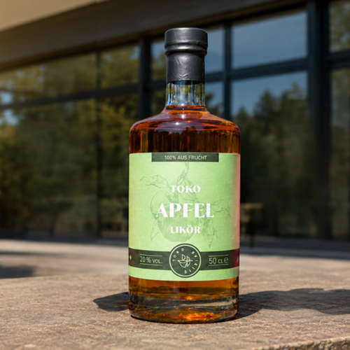Flasche Toko Rote Apfel auf einem Steintisch im Freien vor einer modernen Glasfassade im Sonnenlicht, 100 % aus Frucht, 20 % vol., 50 cl