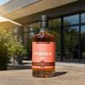 Flasche Toko Pfirsich Likör auf einem Steintisch im Freien vor einer modernen Glasfassade im Sonnenlicht, 100 % aus Frucht, 20 % vol., 50 cl